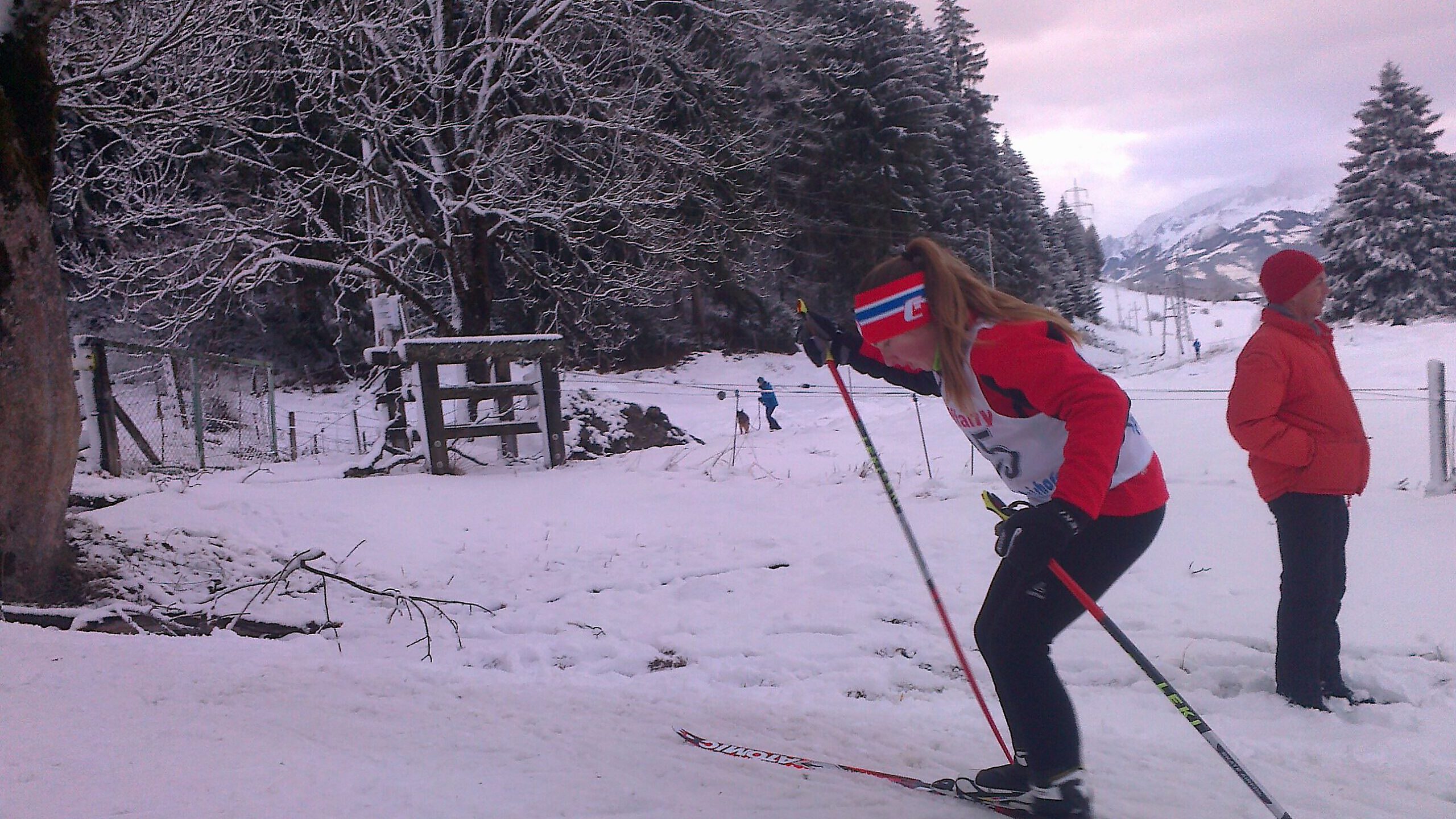 Skilangläuferin bei einem Wettbewerb im Schnee, Zuschauer im Hintergrund. Skiclub-Event in Maishofen.