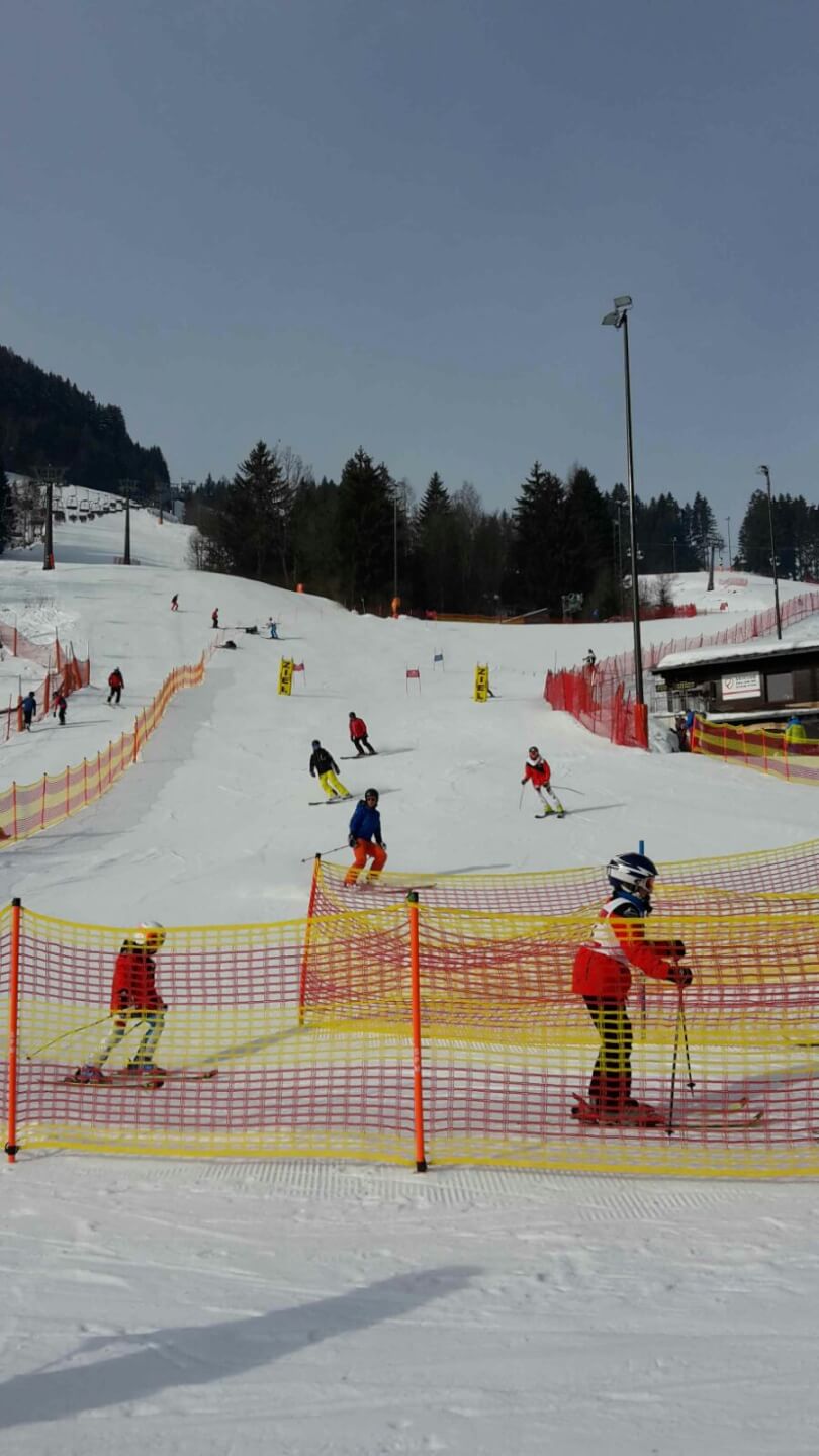 Kinder beim Skifahren im Wettbewerb auf einer Piste in Zell am See mit Absperrungen.