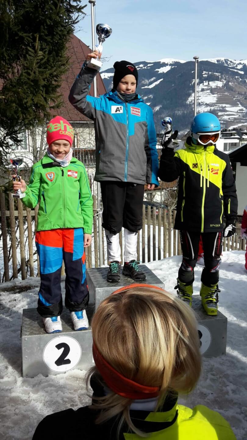 Drei Kinder mit Pokalen auf dem Siegerpodest beim Kindercup Mini Cross in Zell am See.