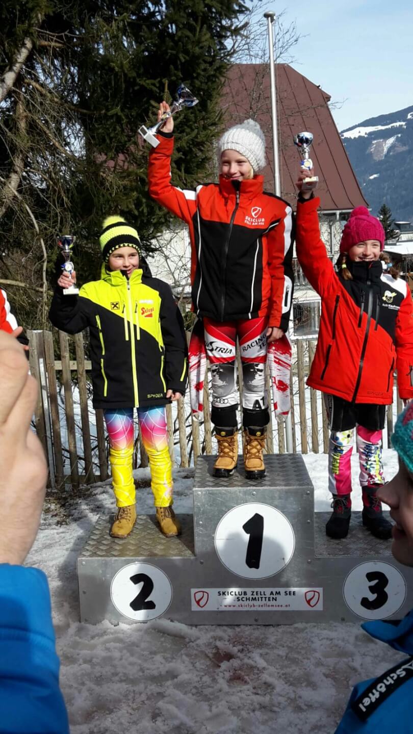Drei Kinder stehen auf dem Siegertreppchen beim Kindercup in Zell am See und feiern.