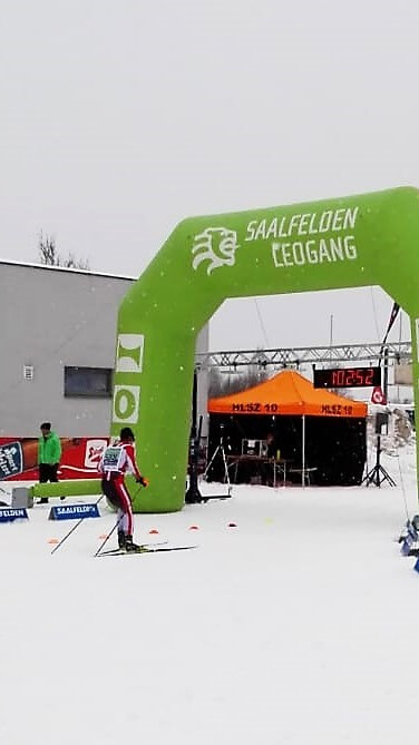 Starttor des Saalfeldener Skimarathons mit Läufern im Schnee und Zeitmessung im Hintergrund.