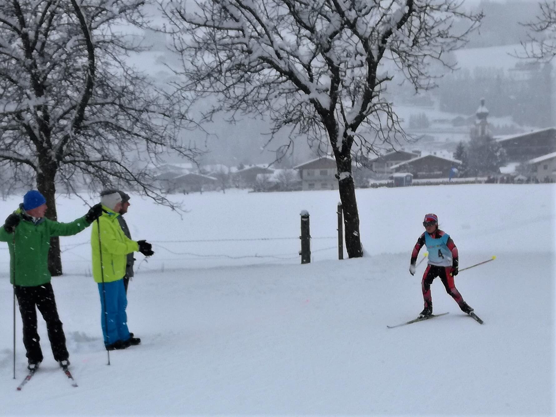 Ein Kind nimmt an einem Skirennen im Schneefall teil, begleitet von Zuschauern.