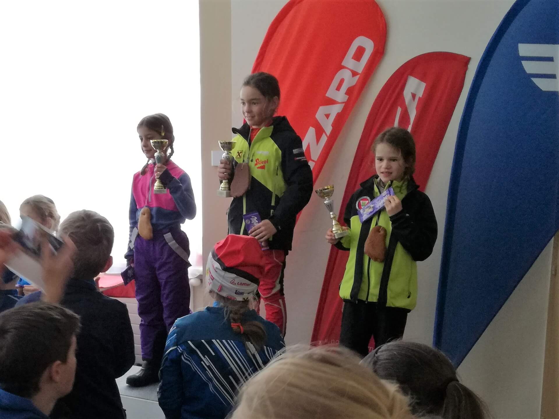Drei Kinder mit Pokalen stehen auf dem Siegertreppchen beim BC Skating in Mittersill.
