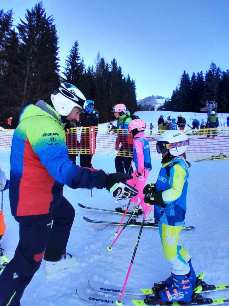 Trainer gibt Tipps an junge Skifahrer beim KC-Rennen in Hinterglemm, Schnee und Bäume im Hintergrund.